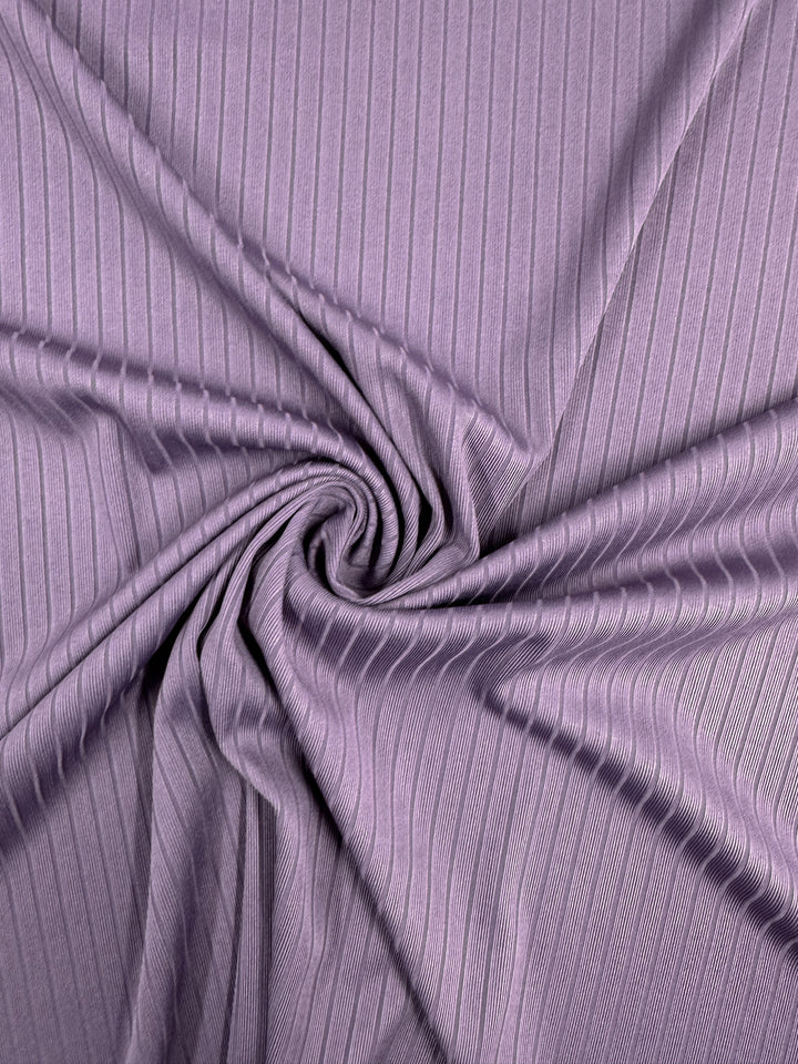 Close-up of Rib Knit - Grape Compote - 170cm by Super Cheap Fabrics, featuring a central spiral pattern in lavender. Textured vertical lines add movement and depth, showcasing the medium weight fabric's versatile stretch.