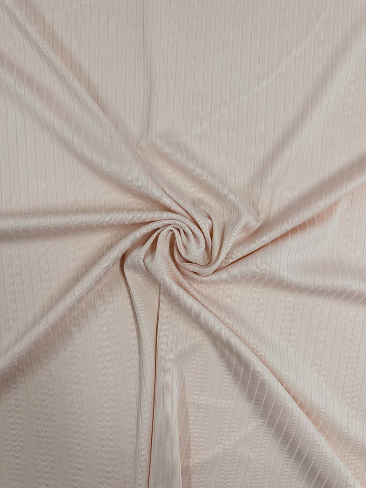 A close-up of the Super Cheap Fabrics' Rib Knit in Creole Pink, 168cm wide, reveals medium-weight fabric with subtle vertical pinstripes. It gathers at the center to form a swirl pattern, showcasing its stretchy material that drapes smoothly into soft folds and waves.