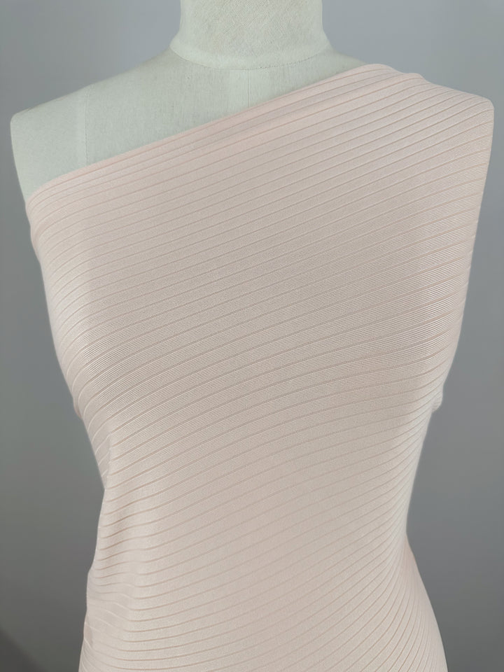 Close-up of a Creole Pink Rib Knit top by Super Cheap Fabrics on a mannequin. The medium-weight, one-shoulder stretchy fabric features a textured pattern, perfectly covering the torso. The background is neutral and out of focus.