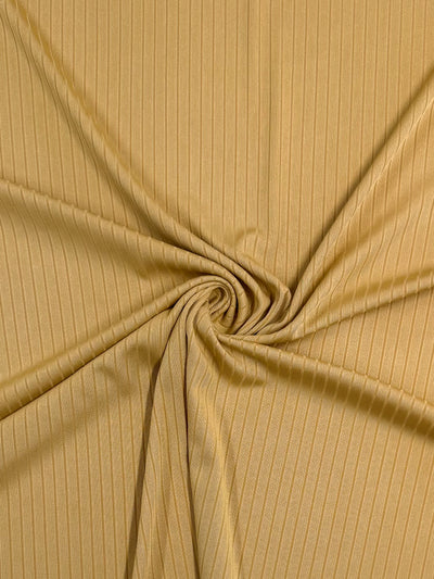 Close-up of the Rib Knit - Pale Golden Nugget fabric by Super Cheap Fabrics, 173cm wide. The light brown material is neatly gathered at the center into a circular twist, appearing soft with a subtle vertical line pattern.