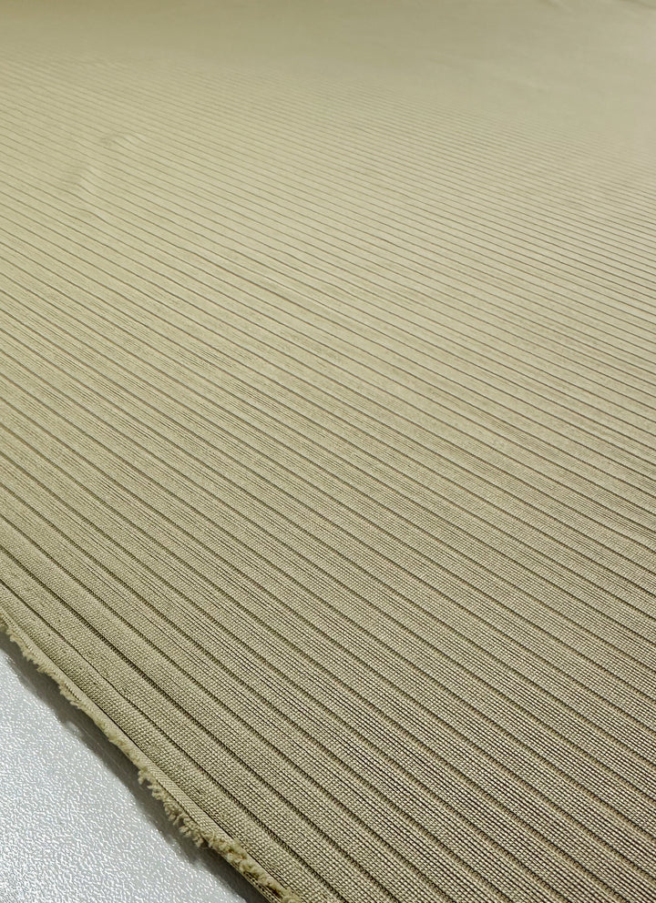 A close-up of the Super Cheap Fabrics' Rib Knit - Hay (170cm) shows its textured, medium-weight ribbed beige material with slightly frayed edges on a smooth, light-colored surface.