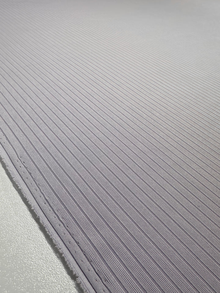 Close-up of Super Cheap Fabrics' Rib Knit - Thistle - 175cm, featuring medium weight rib knit with diagonal ridges. The light gray fabric is slightly reflective, and the edge is visible on the left side.