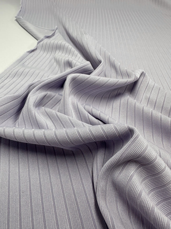 A close-up of Super Cheap Fabrics' Rib Knit - Thistle shows its light gray, medium-weight fabric with vertical ribbed lines creating a wavy, textured drape.