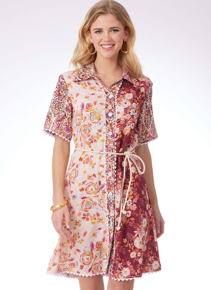 A smiling woman is dressed in a knee-length, half-sleeve outfit featuring floral patterns in shades of pink and maroon. This Lycra-infused dress is designed with a collar, button-down front, and complemented by a rope belt. She adds hoop earrings and a bracelet to her ensemble while posing against a plain background. The look perfectly showcases the design from Super Cheap Fabrics’ Pattern - Mccall's - M8395 - Misses’ Dress, Top and Trousers collection.