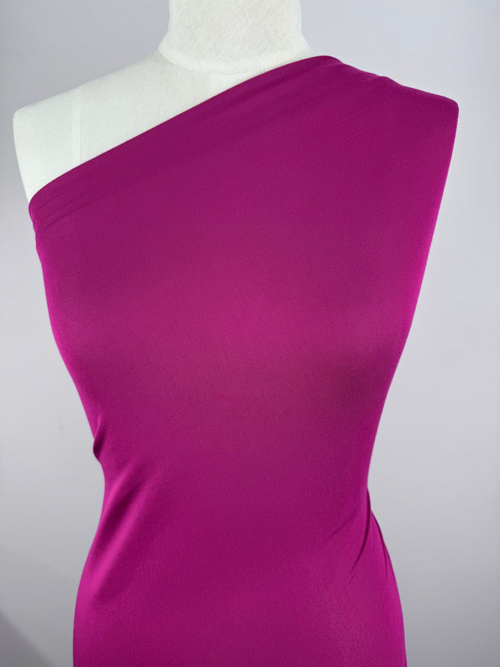 A mannequin displays an elegant one-shoulder dress made from Super Cheap Fabrics' Cotton Lycra in Festival Fuschia. The smooth, form-fitting design exudes sophistication against a neutral gray background.