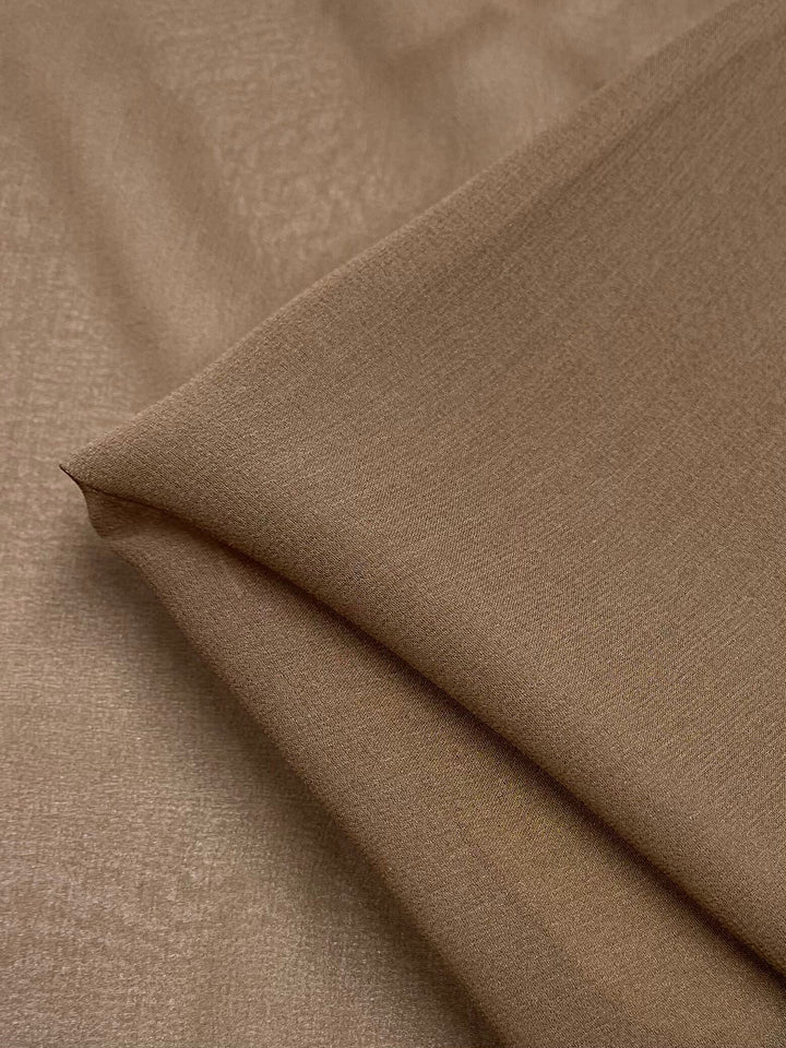 A close-up image of folded Silk Georgette in the Bark colorway, 135cm wide, from Super Cheap Fabrics. The fabric is neatly layered, showcasing its soft and slightly shiny surface. This lightweight georgette is perfect for spring and summer outfits. The lighting highlights the fine weave and even color, giving it a warm and elegant appearance.