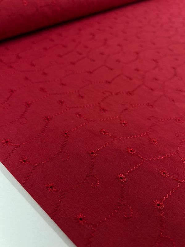 A close-up of the Embroidered Cotton - Dash - 112cm from Super Cheap Fabrics showcases its elegant red roll adorned with delicate floral embroidery. Crafted from natural cotton fibers, the fabric features small embroidered flowers and wavy stitched lines that enhance its textured appearance.