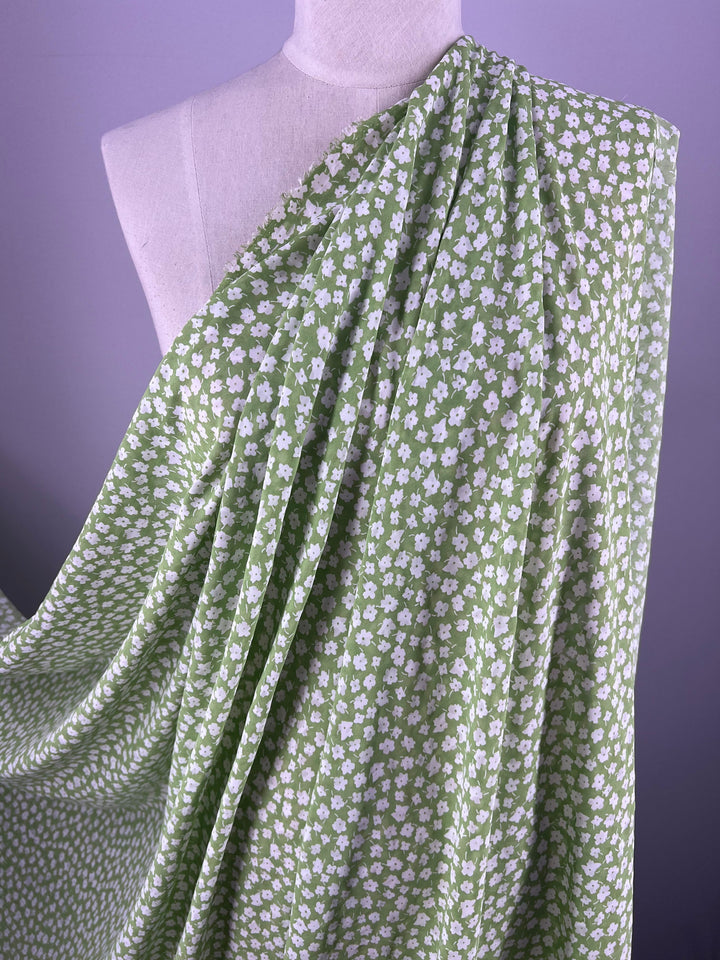 Super Cheap Fabrics' Salt Shrunk Print - Jassy - 155cm, a light green fabric with small white florals from our latest collection, elegantly drapes over a dress form against a neutral purple background.