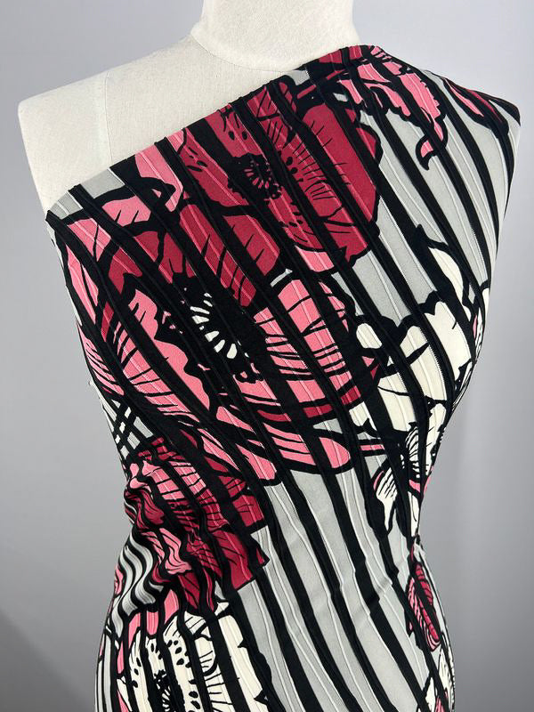 The mannequin displays Super Cheap Fabrics' Textured Lycra - Poppy Dream (150cm), featuring bold red and black floral patterns with vertical black and white stripes in a striking one-shoulder design.