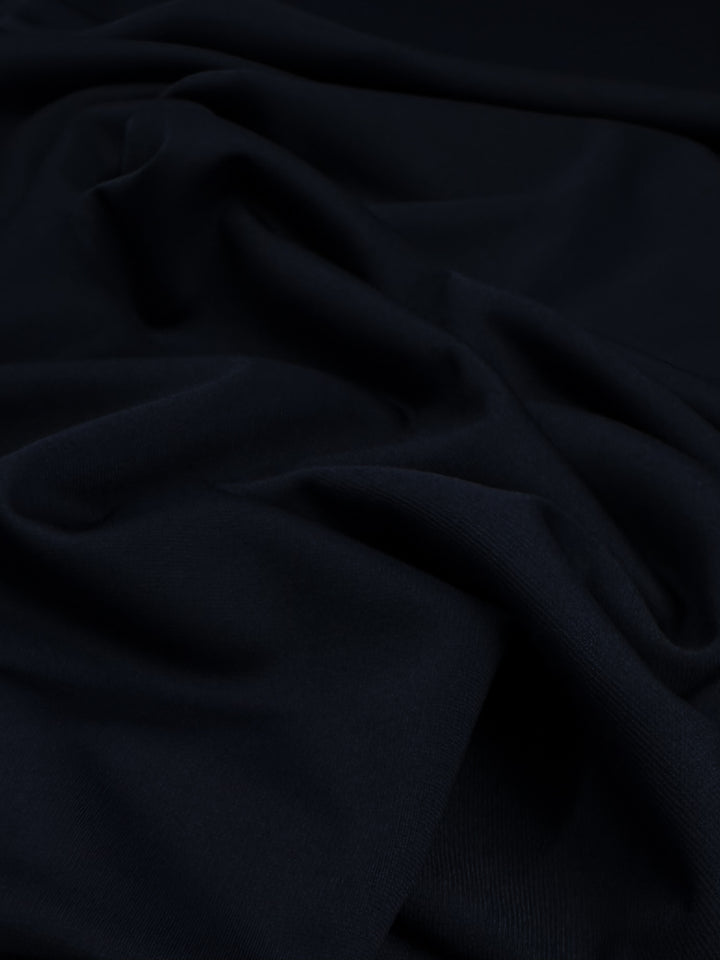 A close-up of soft, intricately folded navy fabric with a smooth texture and subtle shadows, reminiscent of knit fabric, creating a sense of depth and elegance. This is the Ponte - Navy Blazer from Super Cheap Fabrics, measuring 155cm in width.