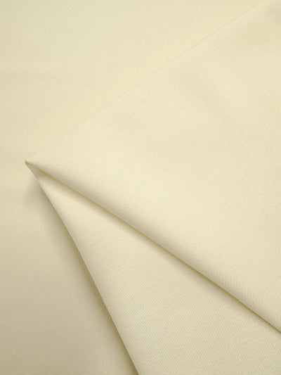 Close-up of Super Cheap Fabrics’ Cotton Voile - Cream - 145cm: neatly folded, smooth and slightly lustrous cotton, layered on a matching background—ideal for refined home decor accents.