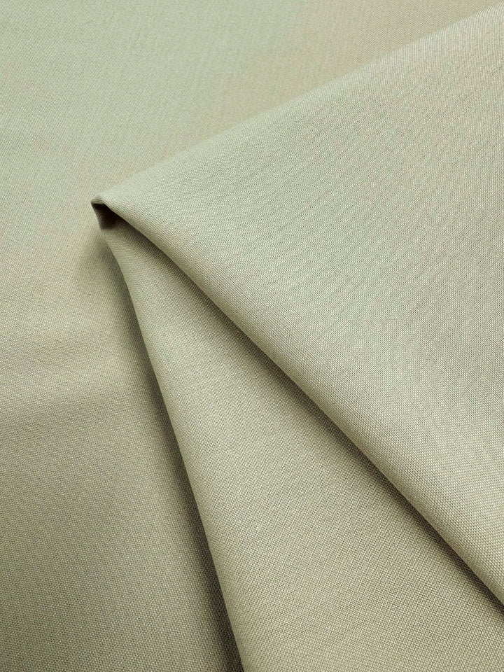 A close-up of Deluxe Suiting - Brown Rice (150cm) by Super Cheap Fabrics shows light beige, medium weight polyester fabric, neatly folded with a smooth texture and subtle brown rice weave.
