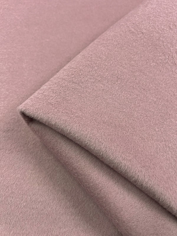 Close-up view of a folded piece of soft pink Wool Cashmere - Zephyr fabric by Super Cheap Fabrics. The texture appears smooth and plush, with slight shadowing where the material is creased. Dry clean only for best care.