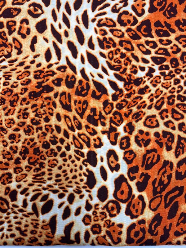 A close-up image of the Textured Deluxe Print - Leo - 155cm from Super Cheap Fabrics. This dynamic and intricate designer fabric features a leopard print pattern with various shapes and sizes of black and dark orange spots set against a background of lighter orange, beige, and white areas.