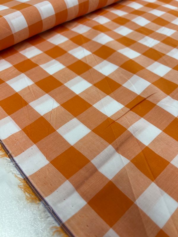 Here's a description using the given product data:

Close-up of the Cotton Gingham XL fabric in orange from Super Cheap Fabrics, featuring a white and orange checkered pattern, laid out flat. This 112cm wide cotton fabric has an even texture with perfectly aligned squares, subtly reflecting light to highlight its sheen. Ideal for infusing charm into your home decor.