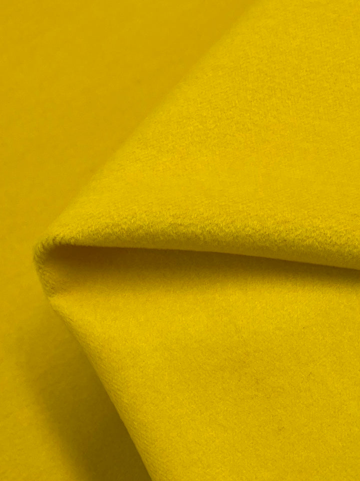 A close-up image of Wool Cashmere - Daisy from Super Cheap Fabrics, showcasing a folded section of the bright yellow fabric. The texture looks soft and smooth, indicative of its medium weight composition.