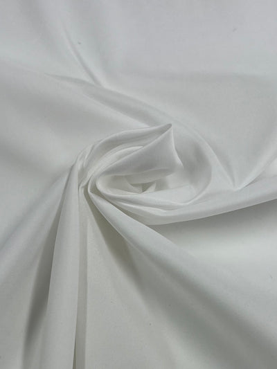 A close-up image of a white fabric with a smooth texture, twisted gently at the center to form soft folds and a subtle spiral design. The lightweight Lining - White - 150cm from Super Cheap Fabrics creates an elegant, minimalistic aesthetic perfect for refined tailoring.