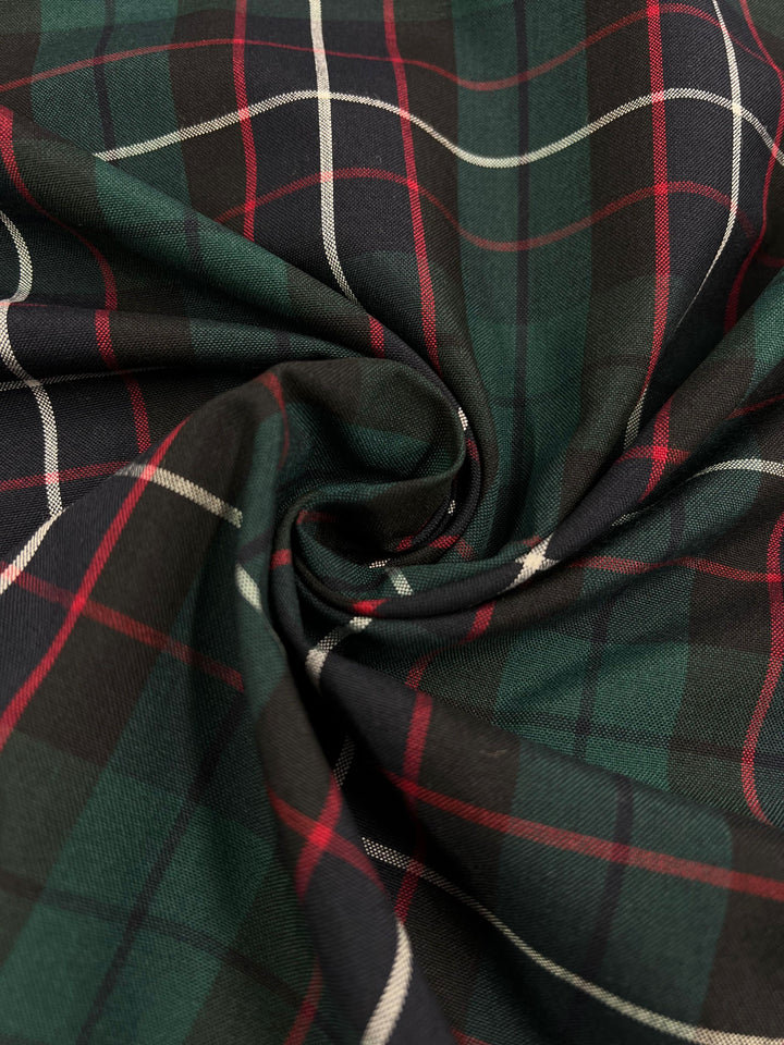 The close-up image showcases a swirl pattern in a green and black tartan fabric, accentuated by subtle thin red and white lines. This lightweight fabric, crafted from a versatile polyester-rayon blend, is perfect for various applications. It is known as "Shirting - Hills - 145cm" and is offered by Super Cheap Fabrics.