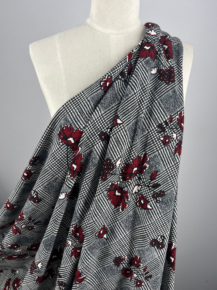 A mannequin draped with the Super Cheap Fabrics' Scuba Crepe - Hounds Dream, a fabric featuring a black and white checkered design adorned with red flowers, is set against a plain gray background.