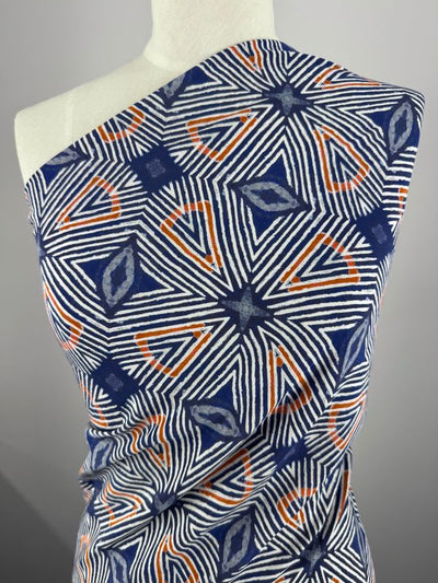 Super Cheap Fabrics' Viscose Satin - Batik (132cm) showcases a geometric design on a mannequin. The blue, orange, and white stars formed by converging lines and circular motifs create a dynamic look perfect for garment lining.