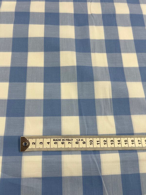 A close-up image showcases the Cotton Gingham XL - Windsurfer fabric from Super Cheap Fabrics, featuring a blue and white checkered pattern. A metal ruler is placed at the bottom, displaying measurements in centimeters from 0 to 13, emphasizing the fabric’s evenly sized squares and its lightweight, natural texture.