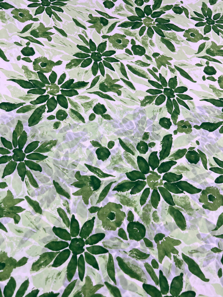 The Salt Shrunk Print - Edelweiss - 155cm by Super Cheap Fabrics features vibrant green leaves and flowers on a textured, light background. The dense clusters of foliage and floral shapes offer a lively, natural look to this elegant fabric.