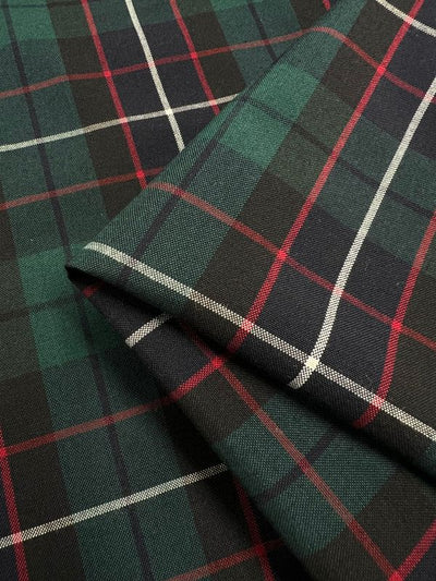 A close-up view of the folded Shirting - Hills - 145cm from Super Cheap Fabrics reveals a lightweight fabric with a tartan pattern in dark green, black, red, and white stripes. Made from polyester rayon, this classic plaid design offers a textured and traditional look, making it ideal for various applications.