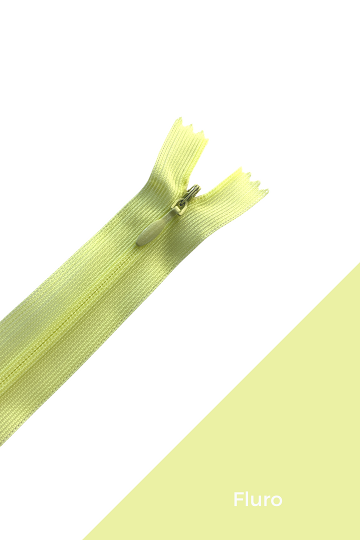 Image of a light yellow zipper on a white and yellow gradient background. The word “Fluro” is printed in the bottom right corner. The partially open zipper, revealing its teeth and slider, hints at an invisible zipper design, ensuring a durable and elegant finish. This is the 30cm Invisible Zip in Yellows & Oranges by Super Cheap Fabrics.