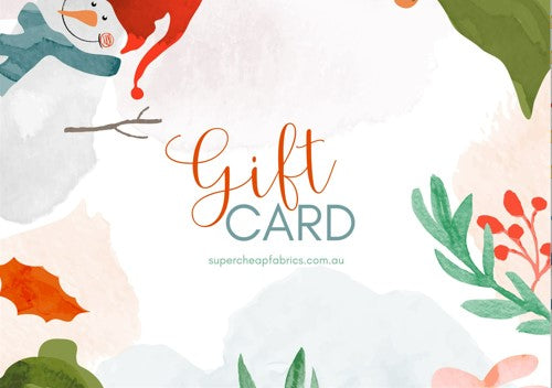 A festive Super Cheap Fabrics Gift Vouchers features decorated text reading "Gift Card" in orange and teal. The design includes a smiling snowman with a red hat, green foliage, red berries, and autumn leaves. Perfect for any sewing enthusiast, you can redeem it online at supercheapfabrics.com.au.