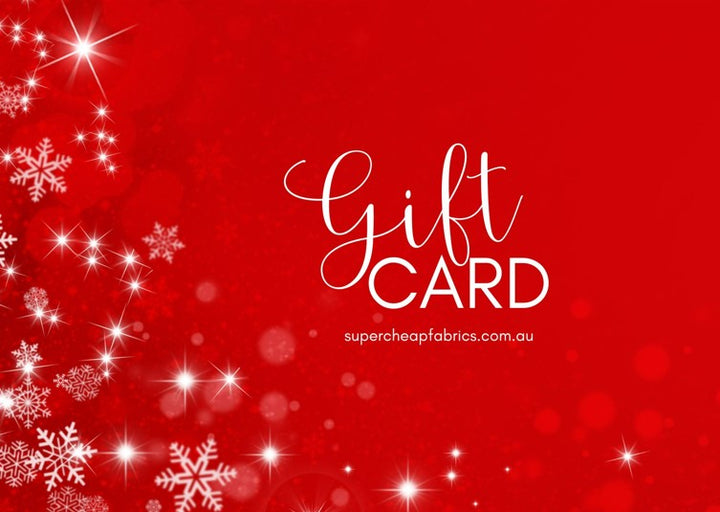 A festive Super Cheap Fabrics Gift Voucher with a bright red background, white snowflakes, and sparkles. The text "Gift Voucher" is prominently displayed in elegant white script, along with the website "supercheapfabrics.com.au" in smaller white text. Perfect for any sewing enthusiast to redeem online!