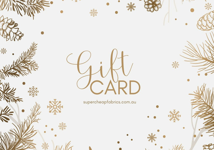 A festive Super Cheap Fabrics Gift Vouchers features golden text reading "Gift Card" with surrounding pine cones, snowflakes, and pine branches in a gold theme, set against a white background. Perfect for the sewing enthusiast, it can be redeemed online at "supercheapfabrics.com.au".