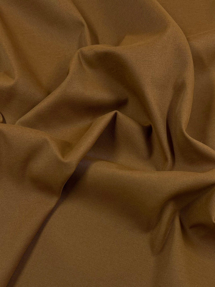 A close-up of Delustered Satin - Caramel Cafe - 150cm from Super Cheap Fabrics with a smooth, soft texture. The material appears to be casually draped and wrinkled, highlighting its fluidity and suppleness. The folds and creases create an interesting pattern of light and shadow, reminiscent of a caramel cafe hue.