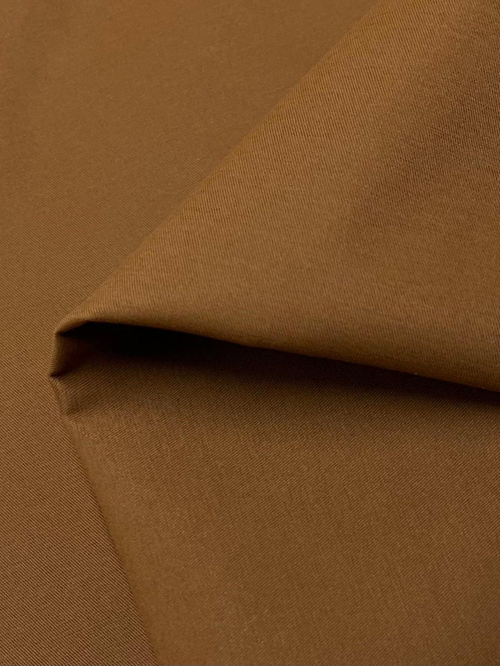 A close-up image of Delustered Satin - Caramel Cafe - 150cm from Super Cheap Fabrics, with a smooth texture and a slight diagonal weave. The fabric is folded at one corner, creating subtle shadows and highlights.