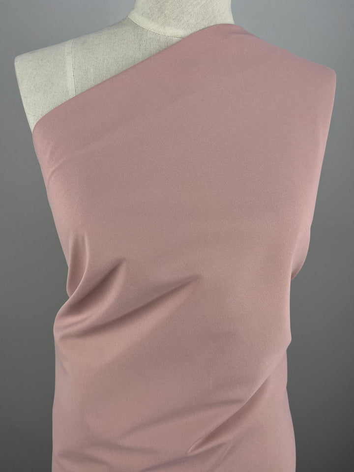 Close-up of a mannequin draped in Delustered Satin - Silver Pink - 150cm by Super Cheap Fabrics. The polyester material has a smooth texture with subtle folds and a shiny finish, showcasing its softness and flow. The background is plain gray, emphasizing the elegance of the garment.