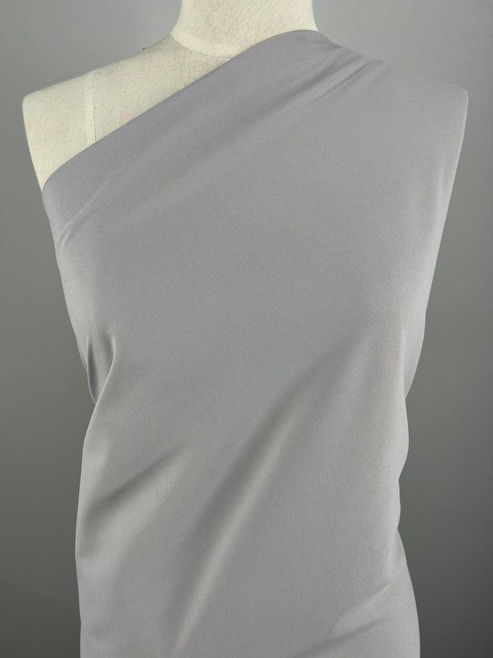 A close-up of a gray, single-shoulder garment draped over a mannequin. Made from 100% Delustered Satin - Raindrops - 150cm by Super Cheap Fabrics, the light-medium weight fabric appears smooth and is wrapped asymmetrically, exposing one shoulder while covering the other, presenting a minimalist and elegant style.