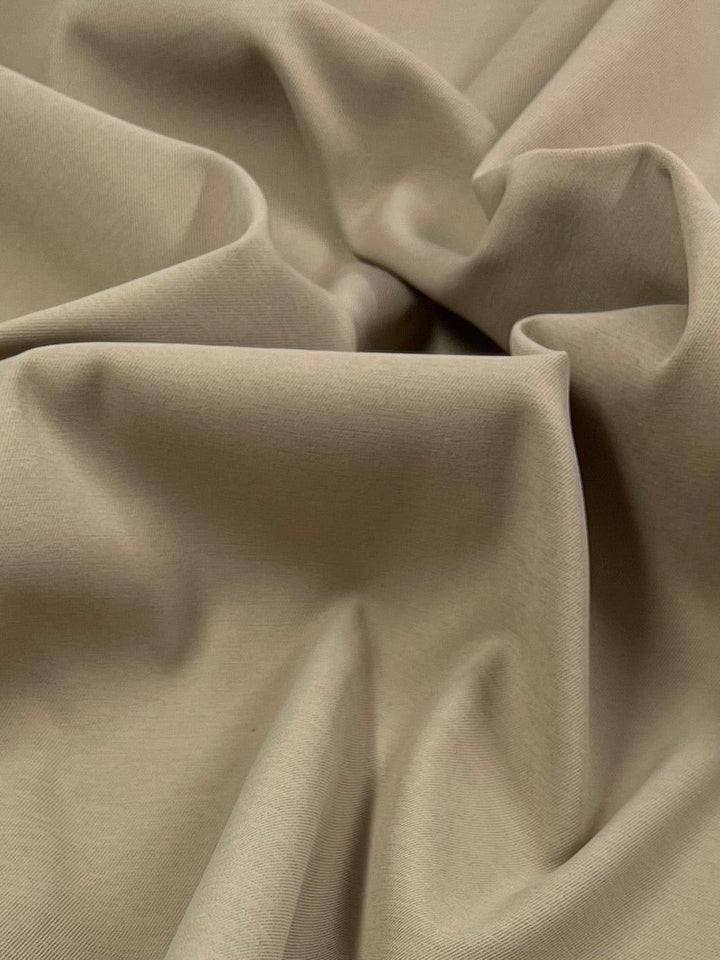 Close-up of beige satin fabric with soft, cascading folds and wrinkles. The material appears smooth and the lighting highlights its texture and gentle draping, showcasing its 150 CM width in all its polyester elegance. The Delustered Satin - Pale Khaki - 150cm by Super Cheap Fabrics is beautifully highlighted.