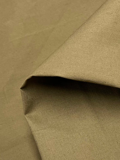 A close-up of a piece of Super Cheap Fabrics' Linen Drill - Butternut - 150cm fabric with a plain, smooth texture. One corner of the fabric is slightly folded over, revealing its underside, which appears identical in texture and color to the top side.