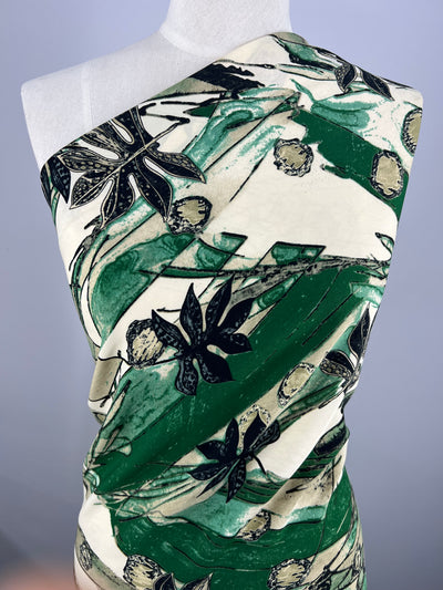 A Deluxe Print - Rebirth - 150cm from Super Cheap Fabrics draped in designer fabric with a nature-inspired print. The versatile polyester features abstract and botanical elements in shades of green, black, and beige. Large, stylized flowers and leaves dominate the design, creating a bold and artistic look.