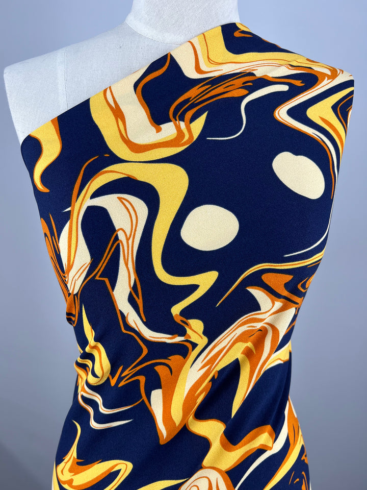 A mannequin showcases a one-shoulder garment made from Super Cheap Fabrics' Printed Crepe - Potion, featuring an abstract pattern of navy blue, yellow, orange, and white swirls on luxurious fabric, enhancing its dynamic and artistic appeal.