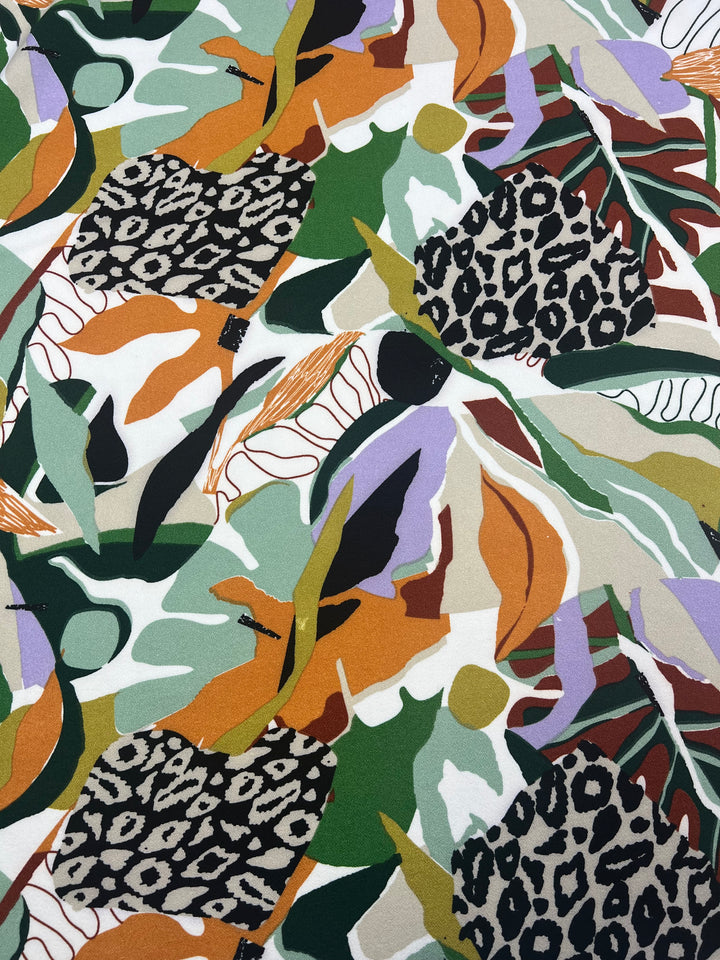 The Printed Crepe - Splash - 150cm by Super Cheap Fabrics showcases a vibrant mix of abstract shapes and botanical elements in green, orange, white, beige, and purple. Interspersed with leopard print sections and delicate line art, this lightweight polyester fabric exudes a dynamic and lively feel perfect for high fashion.