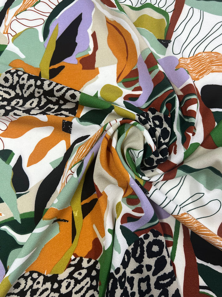 A close-up of Super Cheap Fabrics' Printed Crepe - Splash - 150cm, highlighting its colorful, abstract patterns and lightweight texture. The fabric features diverse shapes and textures, including animal prints with bold green, orange, purple, and black designs. The Polyester fabric is artistically gathered and twisted in the center.