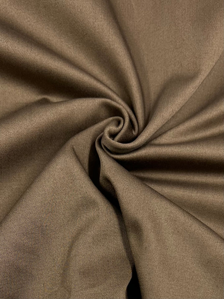 Close-up of a medium-heavy weight, 100% cotton brown fabric, artfully arranged with a central swirl. The smooth material has a soft, slightly glossy texture, catching light on the folds and creating subtle highlights and shadows—perfect for dresses. This is the Cotton Sateen - Carafe - 115cm from Super Cheap Fabrics.