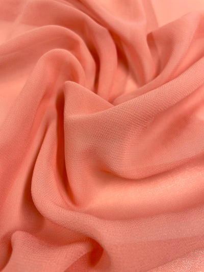 A close-up photograph of soft, flowing Hi-Multi Chiffon - Dahlia - 150cm by Super Cheap Fabrics with a smooth, slightly sheer texture. The lightweight fabric is gently gathered in folds, creating a sense of fluidity and movement. The fine weave of the material is visible, adding to its delicate appearance reminiscent of a blooming dahlia.